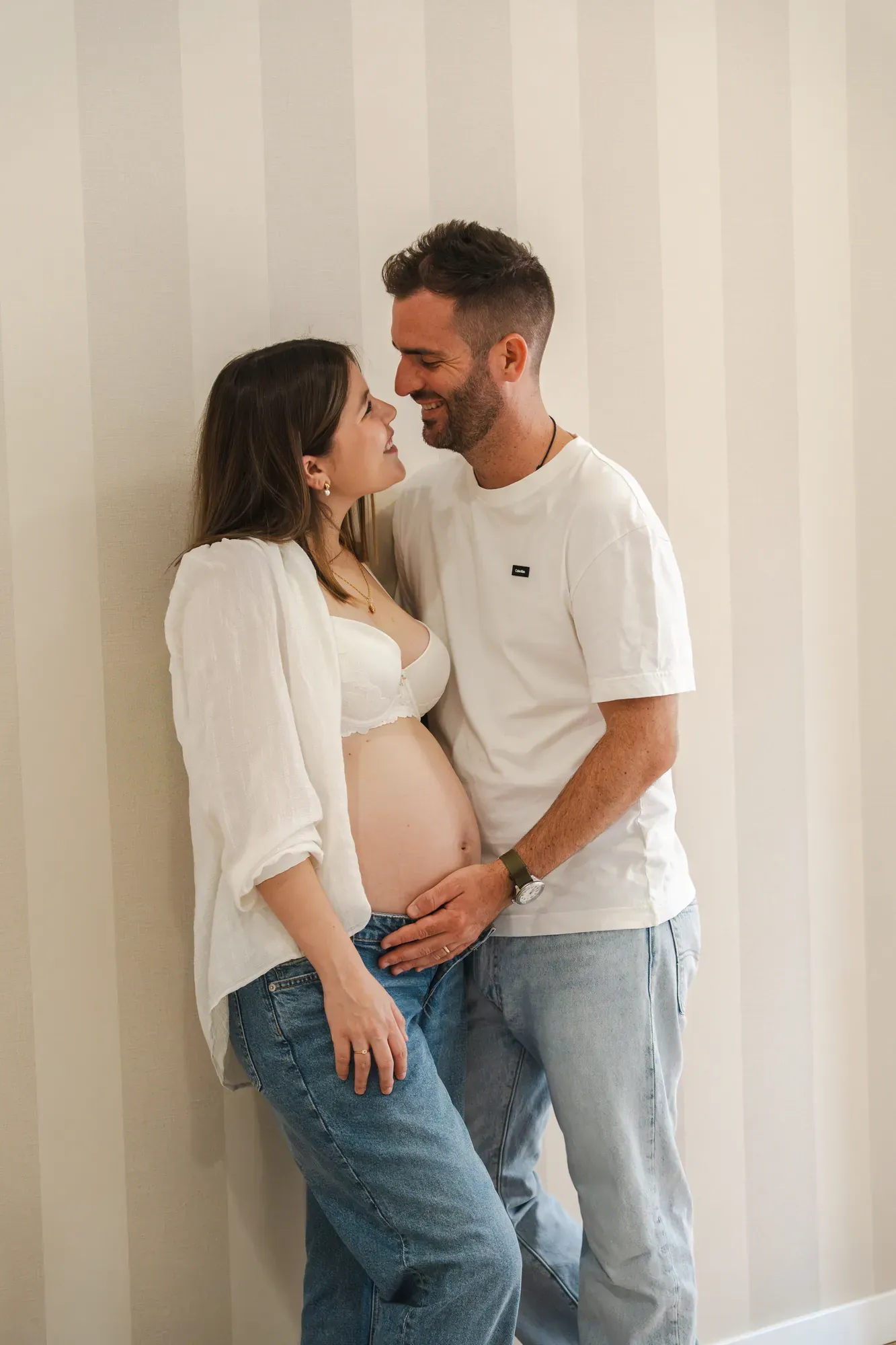 Pareja embarazada sonriéndose junto a una pared de rayas